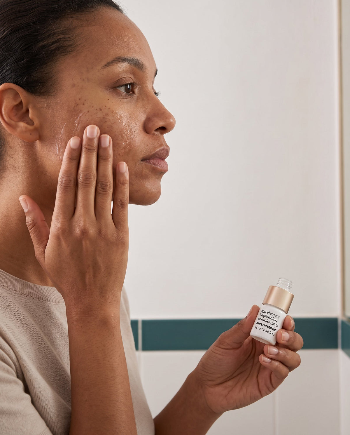 Person applying a pigmentation serum to skin with visible cheek pigmentation in soft morning light.