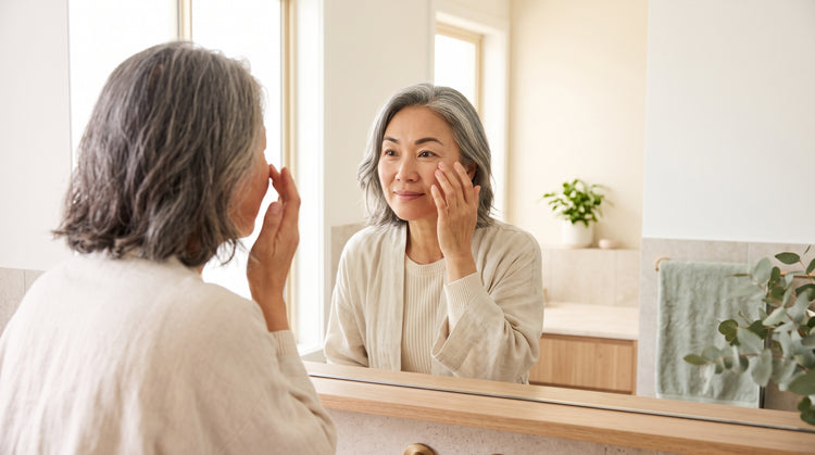 Woman examining dark circles under her eyes in a bathroom mirror in natural morning light