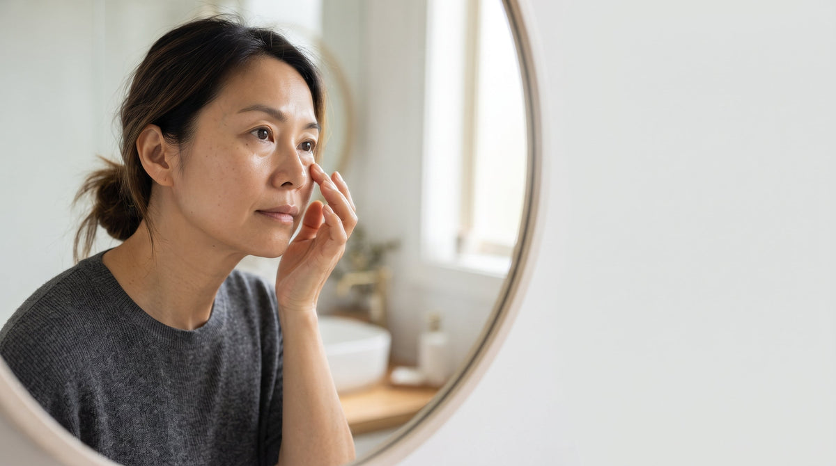 Woman examining her undereye area in a bathroom mirror in soft natural light