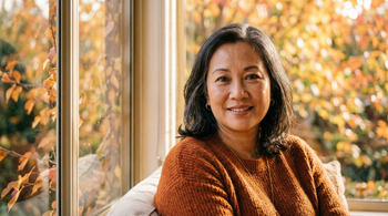 52-year-old East Asian Australian woman with medium skin tone and curvy figure, close-up portrait in warm autumn window light, natural skin texture visible, confident expression