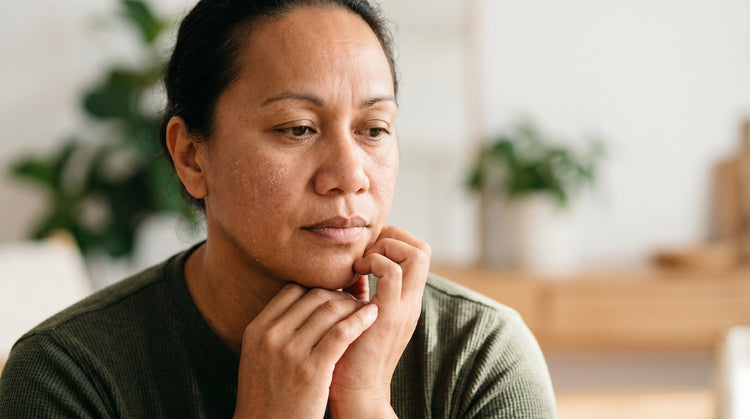 51-year-old Pacific Islander Australian non-binary person with medium skin tone looking down in warm natural light, dry skin texture visible on cheeks